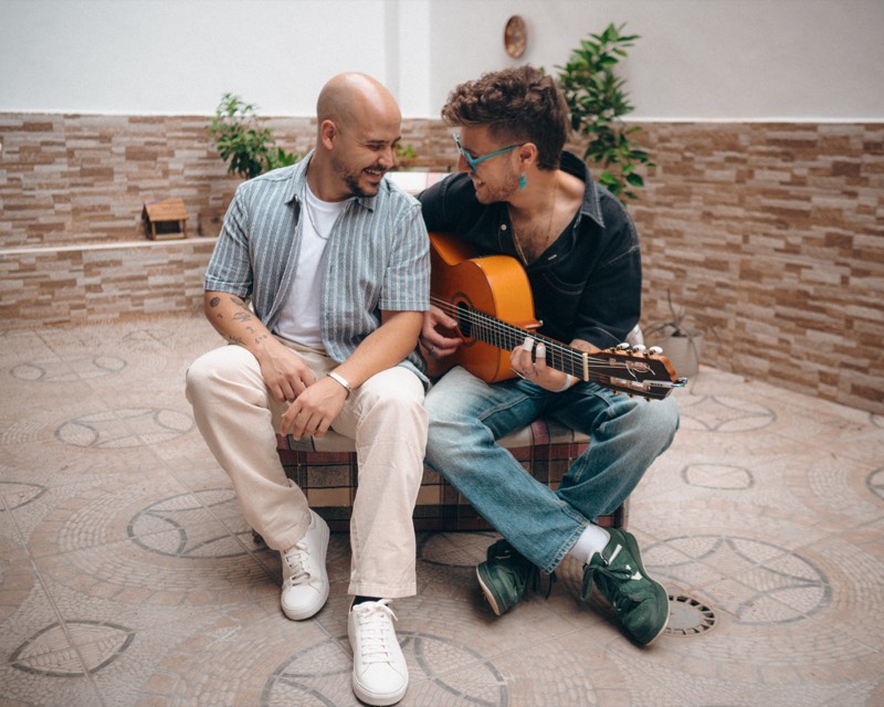 Los dos músicos de PREVARIKE sentados en un patio, uno de ellos con guitarra